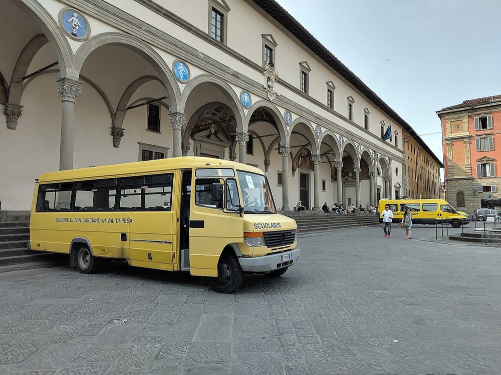 Yellow school buses parked beside an arcaded building in Florence